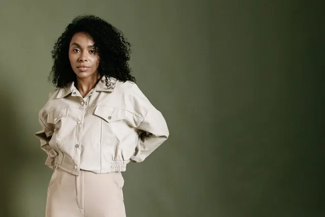 A model in a cream jacket and trousers against an olive backdrop