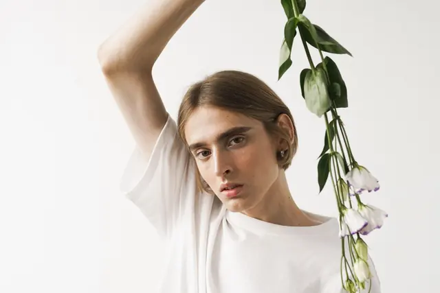 A model in a white t-shirt holding a leafy stem in a white studio