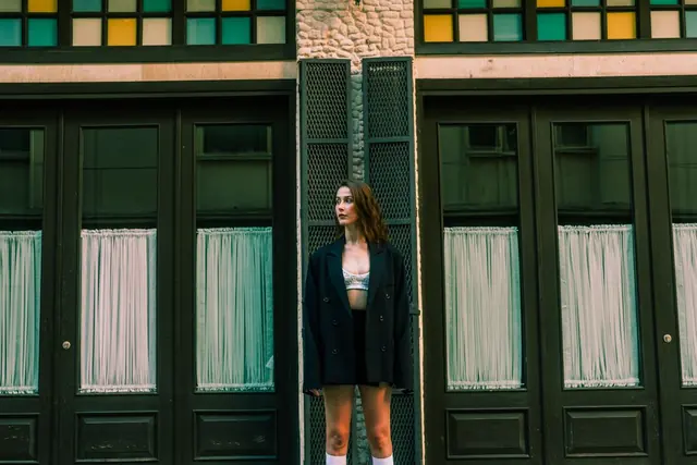 A model in dark layers walking past green doors
